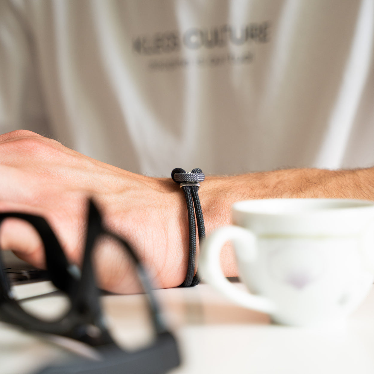 Bracciale Portofino Nereo in paracord grigio indossato al polso con tazza di caffè, Lab93Studio